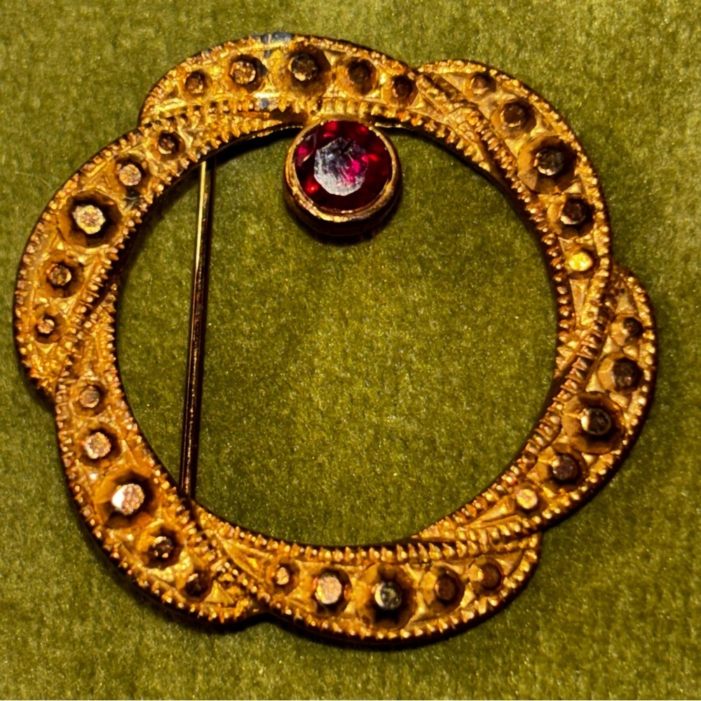 Avon 80s costume jewelry gold tone circle pin with marcasite garnet stone.